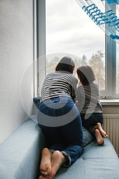 Young mother talking to her little preschooler daughter sitting on the couch looking out the window