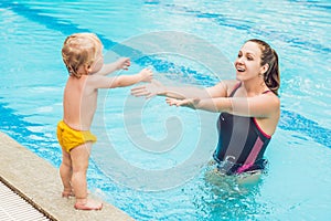 Young mother teach her little son, how to swim in a swimming pool