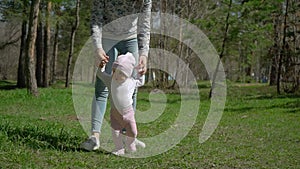 A young mother teaches her daughter how to walk. In the park on the green grass.