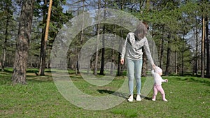 A young mother teaches her daughter how to walk. In the park on the green grass.