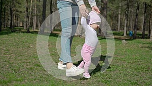 A young mother teaches her daughter how to walk. In the park on the green grass.