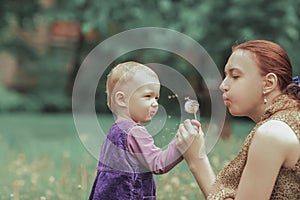 Young mother teaches her little daughter to blow on a dandelion