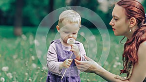 Young mother teaches her little daughter to blow on a dandelion