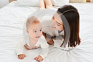 A young mother teaches her newborn son to crawl on the bed