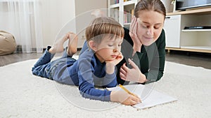 Young mother teaching and helping her son doing homework on floor at home. Concept of domestic education, child