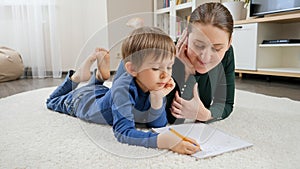 Young mother teaching and helping her son doing homework on floor at home. Concept of domestic education, child
