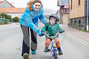 Young mother teaching her 2 years old little son to ride a bike, outdoors.