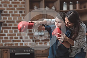 Young mother teaching her little son in boxing gloves how to box