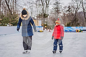 Young mother teaching her little son ice skating at outdoor skating rink. Family enjoy winter on ice-rink outdoors