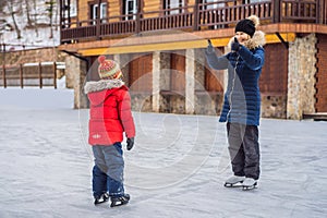 Young mother teaching her little son ice skating at outdoor skating rink. Family enjoy winter on ice-rink outdoors