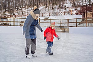 Young mother teaching her little son ice skating at outdoor skating rink. Family enjoy winter on ice-rink outdoors