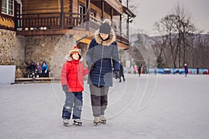 Young mother teaching her little son ice skating at outdoor skating rink. Family enjoy winter on ice-rink outdoors