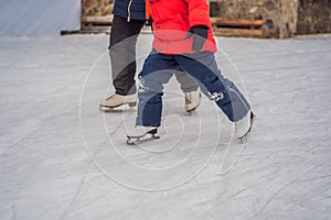 Young mother teaching her little son ice skating at outdoor skating rink. Family enjoy winter on ice-rink outdoors