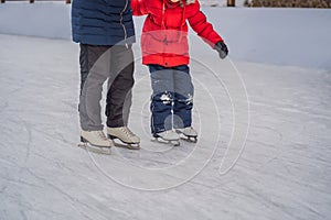 Young mother teaching her little son ice skating at outdoor skating rink. Family enjoy winter on ice-rink outdoors
