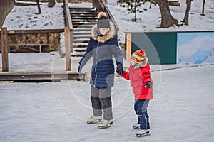 Young mother teaching her little son ice skating at outdoor skating rink. Family enjoy winter on ice-rink outdoors