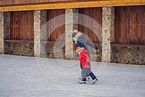 Young mother teaching her little son ice skating at outdoor skating rink. Family enjoy winter on ice-rink outdoors