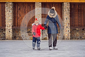 Young mother teaching her little son ice skating at outdoor skating rink. Family enjoy winter on ice-rink outdoors