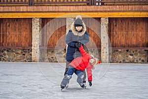 young mother teaching her little son ice skating at outdoor skating rink. Family enjoy winter on ice-rink outdoors