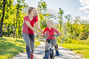 Young mother teaching her son how to ride a bicycle in the park