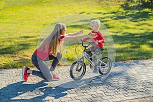 Young mother teaching her son how to ride a bicycle in the park