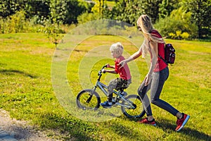 Young mother teaching her son how to ride a bicycle in the park