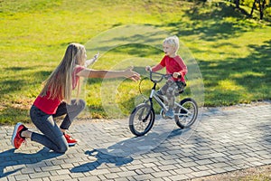 Young mother teaching her son how to ride a bicycle in the park