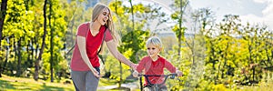 Young mother teaching her son how to ride a bicycle in the park BANNER, LONG FORMAT