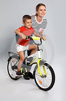 Young mother teaching son to ride bicycle on grey