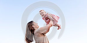 Young mother throws up baby daughter and laughing in the sky. Happy family in the summer outdoors