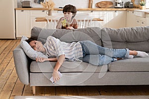 Young mother tired of hyperactive kid. Depressed mom lying on couch stressed with noise need rest