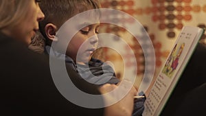 Young mother together little son reading a book lying on bed in cozy bedroom