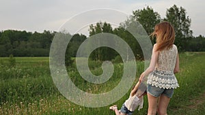 Young mother twists a baby girl on a green field in summer