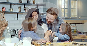 Young mother and two cute children rejoicing to the arrival of dad hugging and kissing while cooking homemade cookies together