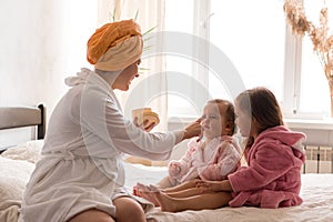 Young mother two daughters in curlers bathrobes. happy smiling family skin care concept. Mom teaches little kids child