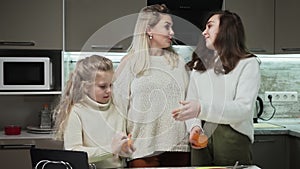 Young mother and two her daughters cooks fruits salad at kitchen. Sisters peels oranges