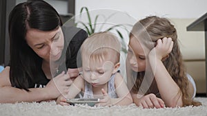 Young mother and two kids having fun with tablet computer on the floor at home, lifestyle.