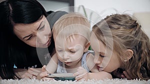 Young mother and two kids having fun with tablet computer on the floor at home, lifestyle.