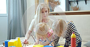 Young mother and two little daughters drawing with colored pencils on paper at home. Leisure, early childhood education