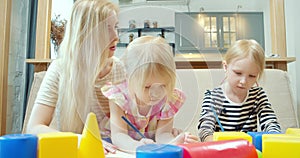 Young mother and two little daughters drawing with colored pencils on paper at home. Leisure, early childhood education