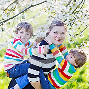 Young mother and two little twins boys having fun in blooming ga