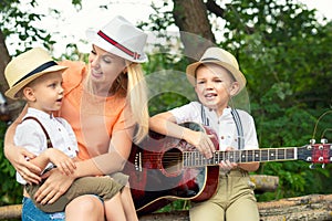 Young mother and two sons are resting in the woods,singing songs with a guitar.