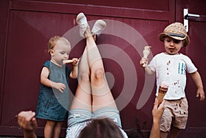 A young mother with two toddler children outdoors in summer, eating ice cream.