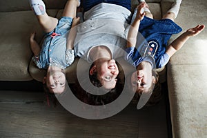 a young mother and two young daughters are lying on the sofa upside down