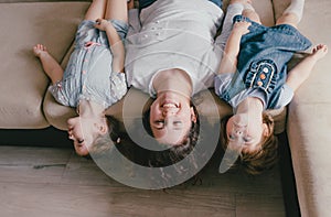 a young mother and two young daughters are lying on the sofa upside down