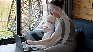 Young mother types on laptop sitting with baby girl on lap