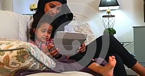 Young mother using a digital tablet with her daughter on the sofa at home 4k