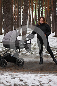 young mother on a walk with her baby. girl with a baby in a stroller in the winter on a walk.