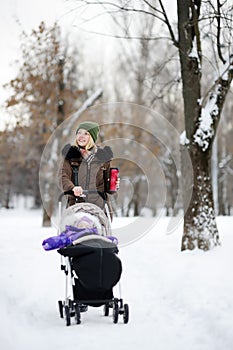 Young mother walking with baby in stroller in winter park