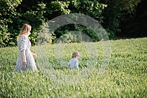 Young mother walking in the field among green grass with her son 3 years old