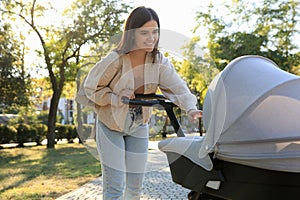 Young mother walking with her baby in stroller at park on sunny day